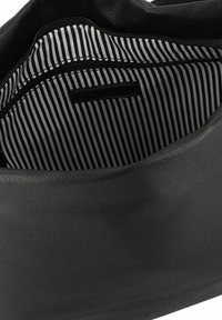 Interno di una borsa in pelle nera con una fodera a strisce bianche e nere, dotata di una tasca con zip e una finitura liscia al tatto.