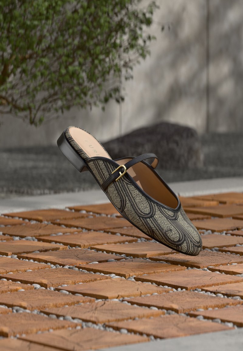 Chaussure slip-on avec motif géométrique noir et beige, bride noire avec boucle dorée, suspendue en l'air au-dessus de carreaux en bois à l'extérieur.