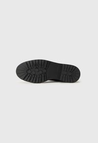 Black rubber sole with a textured tread for grip, featuring circular and linear patterns, designed for durability and traction.