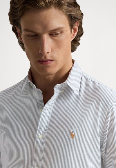 Ανοικτό μπλε και λευκό ριγέ πουκάμισο με κουμπιά και γιακά, με μικρό κεντημένο λογότυπο. Υλικό βαμβακερό με απαλή υφή.