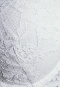 Reggiseno bianco in pizzo con motivi floreali, tessuto testurizzato e bordi lisci, progettato per comfort e una vestibilità sicura.