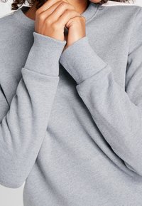 Lichtgrijze trui met geribbelde manchetten en halslijn, met een zachte textuur en een losse pasvorm. De stof lijkt licht en comfortabel.