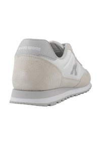 Baskets blanches et gris clair avec un talon en daim, un tissu texturé et un logo contrastant sur le côté et à l'arrière. Semelle en caoutchouc.