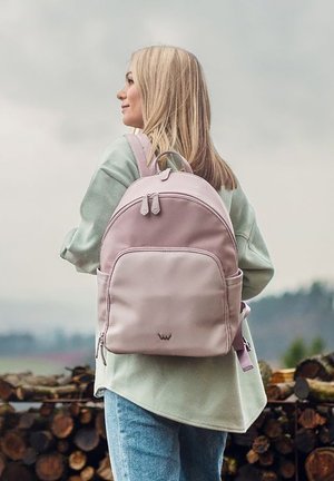 Hellrosa Rucksack mit abgerundeter Form, Vorderfach und verstellbaren Trägern, aus glattem Material, vor unscharfem Außenhintergrund.