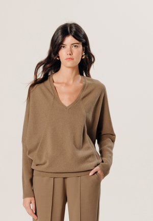 V-Ausschnitt, lockerer brauner Pullover mit gerippten Bündchen und Saum. Weicher Stoff, fällt elegant, getragen mit passenden Hosen.