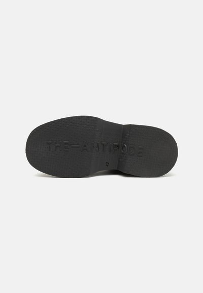 Semelle de chaussure noire avec un caoutchouc texturé, marquage gravé "THE-ANTIPODE" et taille "42" sur une finition mate.