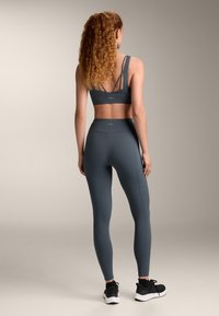 Graues Sportbekleidungsset mit einem enganliegenden Sport-BH mit dünnen Trägern und hochgeschnittenen Leggings. Das Material hat eine glatte, matte Oberfläche.