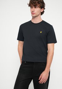 Moška kratka majica z okroglim izrezom v mornarsko modri barvi, izdelana iz bombaža, z majhnim rumenim izvezenim logotipom na prsih.