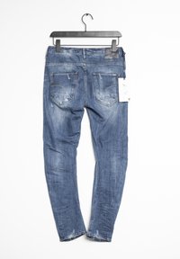 Smal passform blå denim jeans med slitna detaljer, fem fickor och ett lädermärke på midjan. Hängande på en svart klämma.