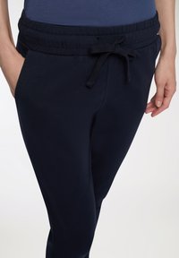 Granatowe dresy z elastycznym pasem i sznurkiem. Gładka tekstura, kieszenie po bokach oraz dopasowany krój wokół kostek.