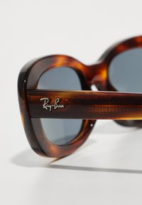 Ochelari de soare Ray-Ban în stil tartan, cu lentile închise, arcuri groase și un logo argintiu pe braț. Textură netedă cu finisaj lucios.
