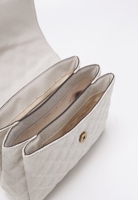 Sac à main blanc matelassé avec une surface texturée, comportant trois compartiments. Fermeture à bouton-pression doré et doublure intérieure lisse.