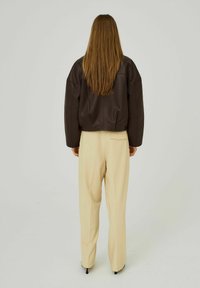 Bruine leren jas met een relaxte silhouet, gecombineerd met beige hoge taille, losse broek. Glad textuur en minimale details zichtbaar.