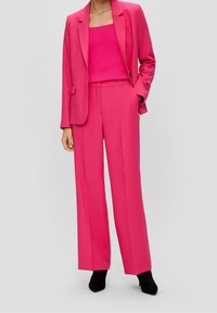 Fuchsia pak met een aansluitende blazer en wijde broekspijpen. Geribbelde top met vierkante hals. Gladde stof met minimaal beslag. Zwarte haklaarzen.