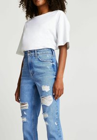Biała bluzka z krótkim rękawem połączona z jasnoniebieskimi, wysokimi jeansami z przetarciami, które mają liczne dziury i postrzępione brzegi.