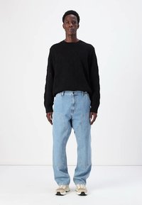 Sort tekstureret strikket sweater med diamantmønster, parret med lyseblå wide-leg denim jeans og lyse sneakers.