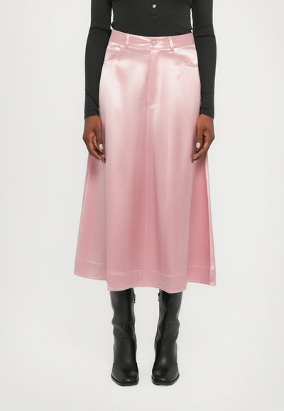 Jupe midi en satin rose avec un design évasé, dotée d'une fermeture à boutons à l'avant et de poches latérales, associée à des bottes noires montant jusqu'aux genoux.