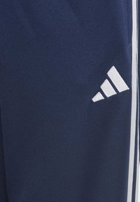 Námorné športové nohavice vyrobené z textúrovanej tkaniny s bielym dizajnom v troch prúžkoch a vyšitým logom na dolnej časti nohavice.