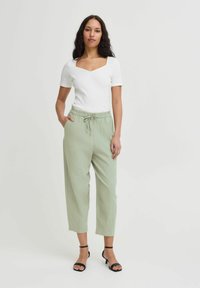 Haut blanc à manches courtes avec encolure carrée, associé à un pantalon vert clair à cordon. Modèle portant des talons noirs à lanières. Design simple.