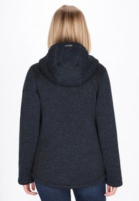 Tmavomodrá mikina na zips s textúrovaným pleteným povrchom, vybavená veľkou kapucňou a zakriveným lemom. Tkanina vyzerá teplá a útulná.