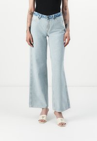Light blue wide-leg jeans made of denim, featuring a blue patterned waistband and front pockets. Smooth texture with visible stitching details.