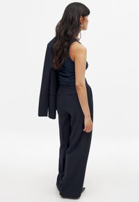 Námornícky modrá bezrukávová blúzka v kombinácii s nohavicami s vysokým pásom a širokými nohavicami. Sako prehodené cez rameno, s čistými líniami a jemnými detailmi pri šití.