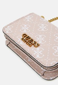 Rosa Kunstleder-Geldbörse mit weißem Logo-Muster, goldfarbenem "GUESS"-Schriftzug, gestepptem Muster und Kettenriemen. Kompakter, rechteckiger Entwurf.
