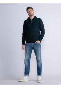 Felpa a maglia blu navy con collo a bottoni, abbinata a jeans azzurri usurati e sneakers bianche. Design casual, in tessuto texture.