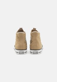 Adidași înalți din pânză bej cu talpă din cauciuc alb-negru. Prezintă detalii cu logo brodat pe partea exterioară și un tab de țesătură pentru tragere.