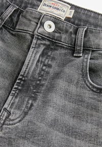 Graue Jeans aus Denim mit Metallknopf, Vordertasche, Gürtelschlaufe und einem weißen Etikett mit der Aufschrift "Denim Goods Co Skinny Fit" Größe 32R.