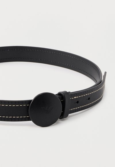 Μαύρη δερμάτινη ζώνη με άσπρα ράμματα και στρογγυλή μαύρη αγκράφα με ανάγλυφο διακριτικό λογότυπο, τοποθετημένη σε λευκό φόντο.