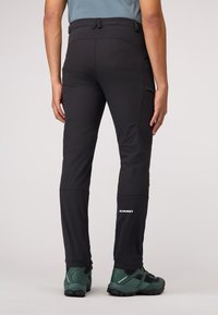 Zwarte outdoorbroek met een gestroomlijnd ontwerp, gemaakt van een duurzame stof, voorzien van een verstelbare tailleband en een wit logo op het onderbeen.