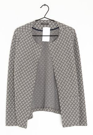 Cardigan à manches longues à motifs noir et blanc, ouvert devant, accroché à un cintre noir avec une étiquette de prix blanche visible.