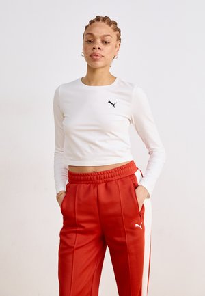 Haut blanc à manches longues coupé avec un logo noir Puma, associé à un pantalon de survêtement rouge avec des bandes blanches sur les côtés et des poches, taille élastique.