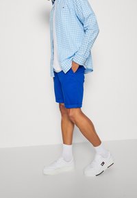 Blå bomullsshorts med uppvikta fållar, tillsammans med en ljusblå rutig skjorta, vit t-shirt, vita strumpor och vita sneakers.