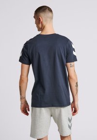 Mörkblå t-shirt med kort ärm och rund halsringning, med vita randdetaljer på axlarna, tillverkad av mjukt bomullsmaterial.