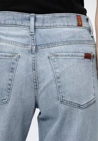 Φωτεινό γαλάζιο τζιν από πίσω, με δύο τσέπες και κόκκινα ταμπελάκια κοντά στη μέση και τη δεξιά τσέπη, σε άτομο που φοράει μαύρο τοπ.