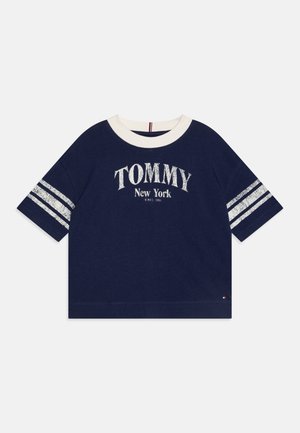 Marine bomull T-skjorte med kremfarget krage, med hvit "TOMMY New York" tekst og sølvstriper på ermene. Korte ermer, avslappet passform.