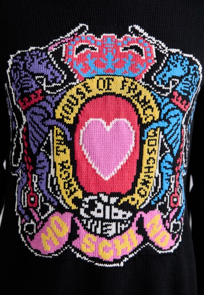 Pull en tricot présentant un design héraldique coloré. Les couleurs dominantes incluent le noir, le rose, le bleu et le jaune. Motif en forme de cœur au centre.