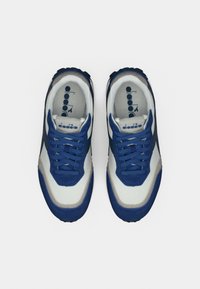 Ζευγάρι μπλε και λευκά αθλητικά παπούτσια Diadora με κορδόνια, από πάνω σε απλό λευκό φόντο.