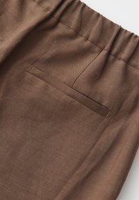 Brown fabric with an elastic waistband and a horizontal welt pocket detail on a garment, showing texture and stitching.