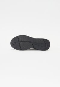 Black sneaker sole with textured rubber, featuring a wave pattern and logo detail, designed for grip and durability.