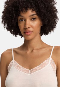 Camisola rosa chiaro con delicata rifinitura in pizzo lungo la scollatura a V e sottili spalline regolabili. Tessuto a coste su tutta la superficie.