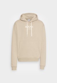 Béžová mikina s kapucí z měkké látky, s přední kapsou, stahovací kapucí a bílým logem uprostřed na hrudi.