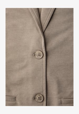 Close-up van een taupekleurige stoffen blazer met twee bijpassende knopen en zichtbare stiksels langs de rever- en zakranden.