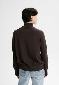 Brauner Rollkragenpullover aus weichem Strick, mit lässigem Schnitt und gerippten Bündchen, kombiniert mit hellblauen Jeans.