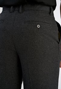 Mörkgrå ullbyxor med en strukturerad yta, som har en enkel bakknapp och två bakfickor. Skräddarsydd passform med en slät midjeresår.