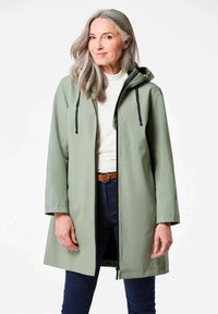 Lichtgroene waterdichte jas met capuchon, voorzijde met rits en verstelbare trekkoorden. Heeft een losse pasvorm en lange mouwen met reflecterende accenten.