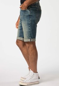 Pantalones cortos de mezclilla con un lavado en azul claro, puños enrollados, cinco bolsillos y un corte clásico, combinados con zapatillas altas blancas.