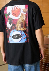Camiseta negra con un gráfico colorido en la parte posterior, que representa un gato dorado, balones de baloncesto y una caja. Material de algodón, corte relajado.